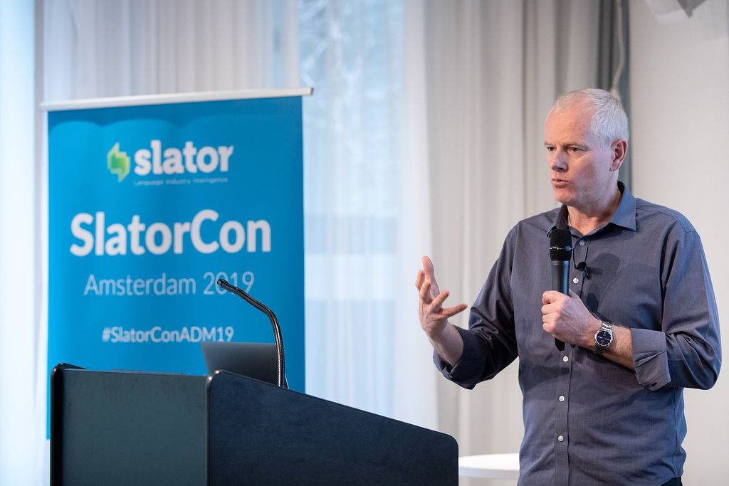 Andrew Bredenkamp speaking into a handheld microphone at SlatorCon Amsterdam in 2019