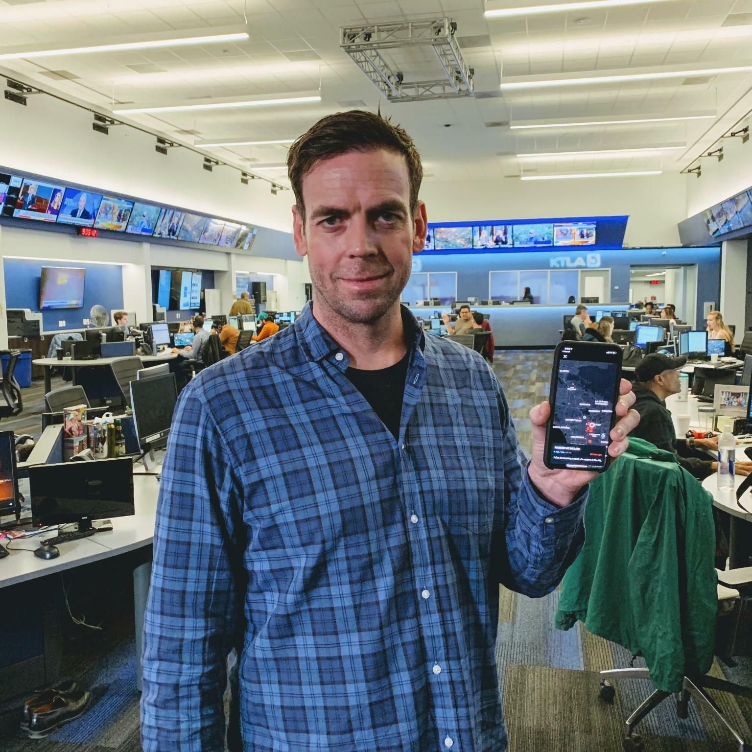 Andrew Frame holding a phone displaying the Citizen app in a television newsroom