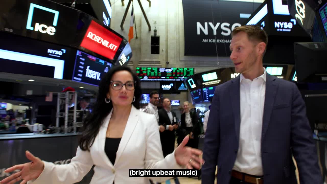 Andrew Hider, right, walking on the New York Stock Exchange floor with interviewer Judy Khan Shaw