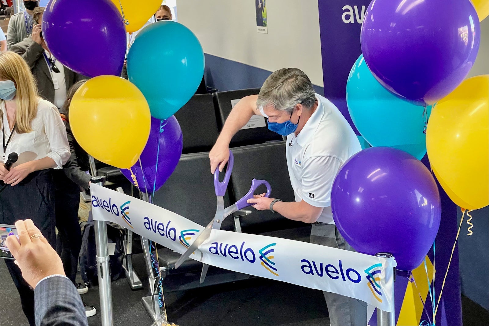Andrew Levy cuts Avelo's inaugural-flight ribbon at Burbank, surrounded by purple, yellow and turquoise balloons.