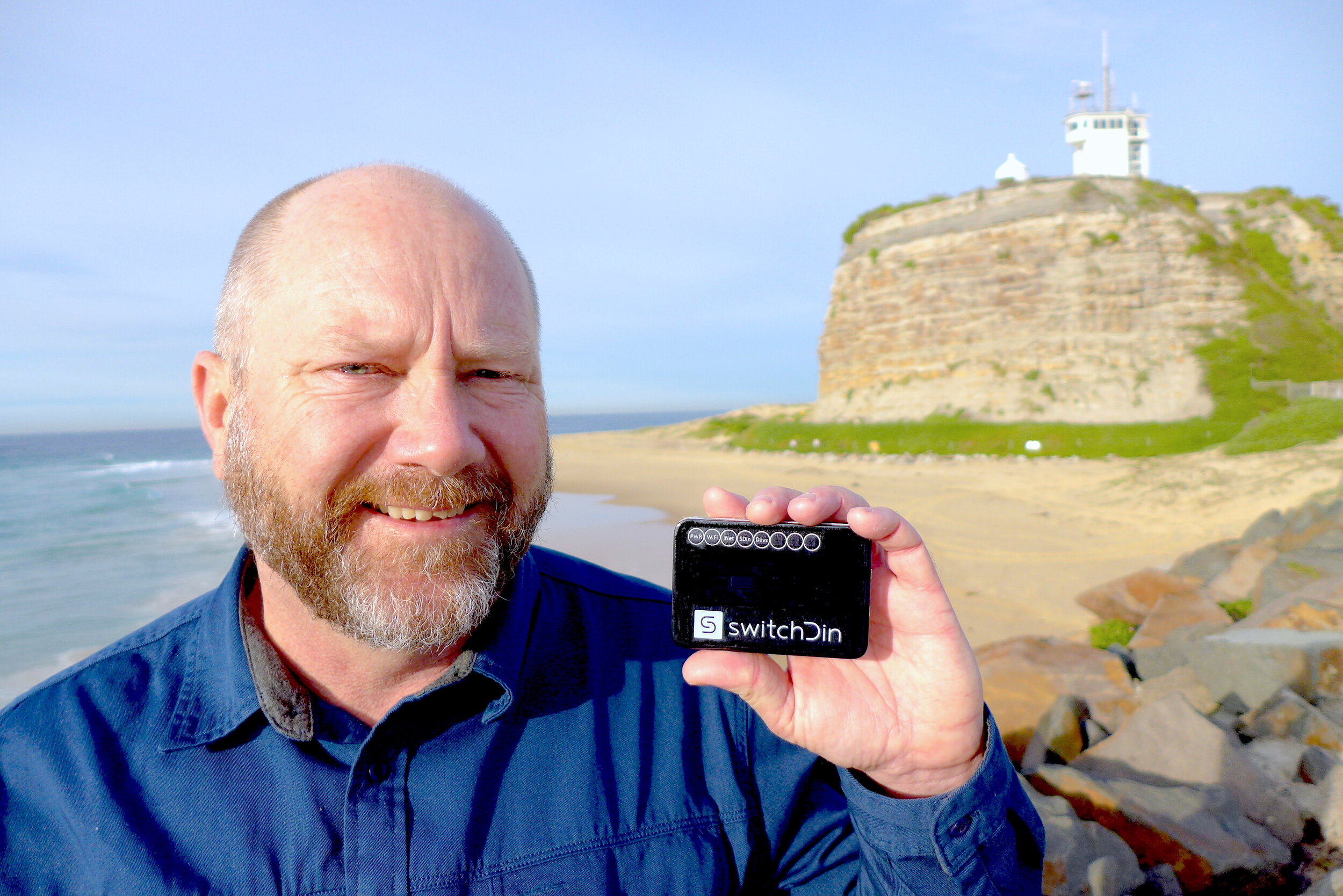 Andrew Mears holding a SwitchDin controller beside the Newcastle coast