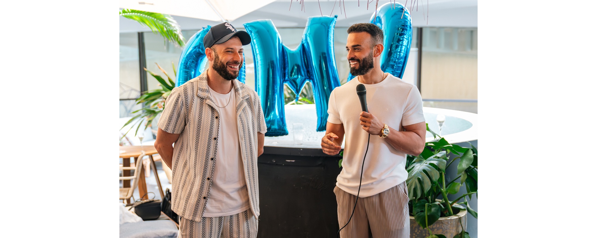 Andrew Raso, right, holding a microphone beside a colleague at an OMG gathering, with blue letter balloons behind them.