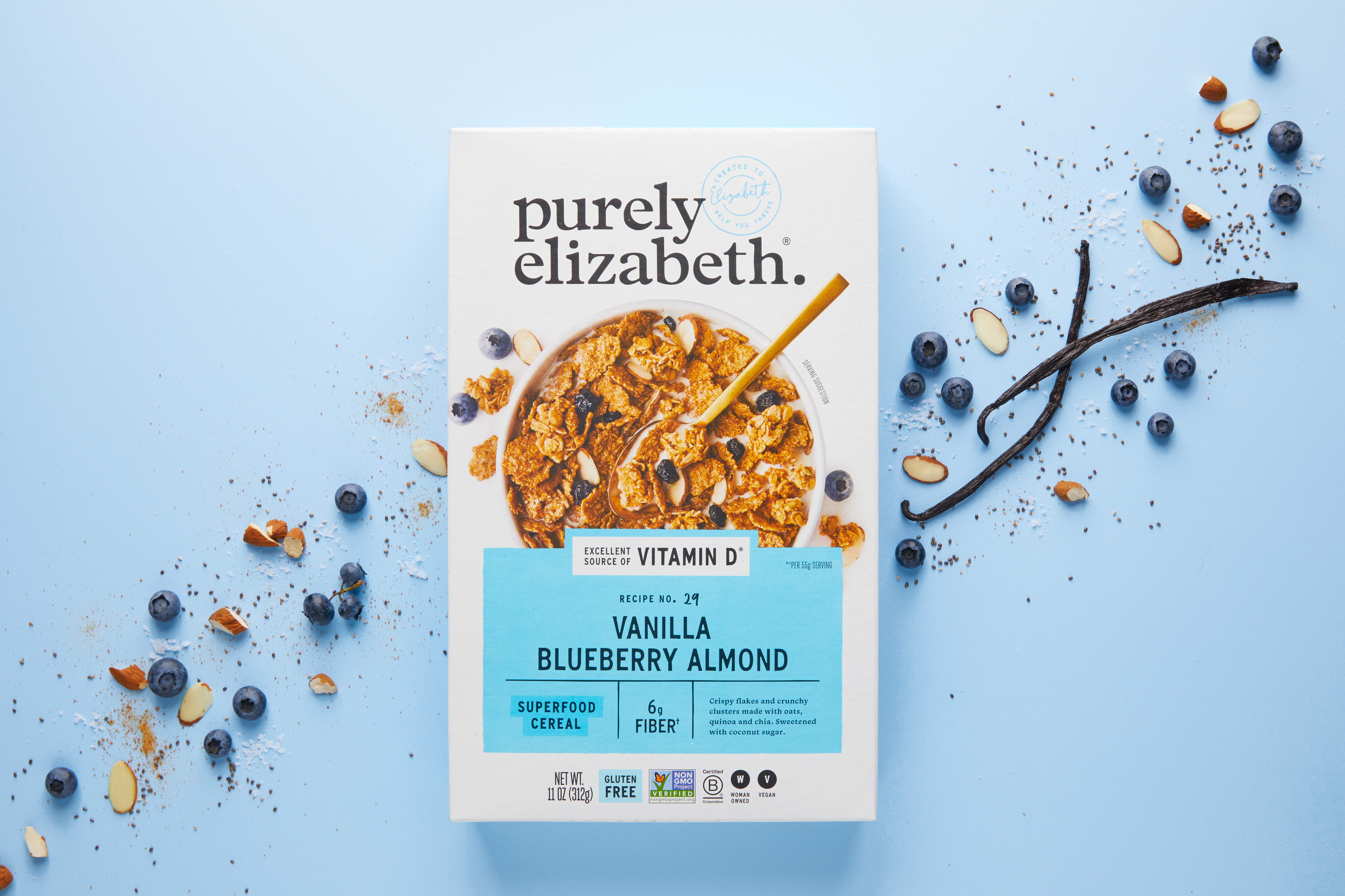 Purely Elizabeth cereal packaging arranged with blueberries, almonds and a spoon on a pale blue background