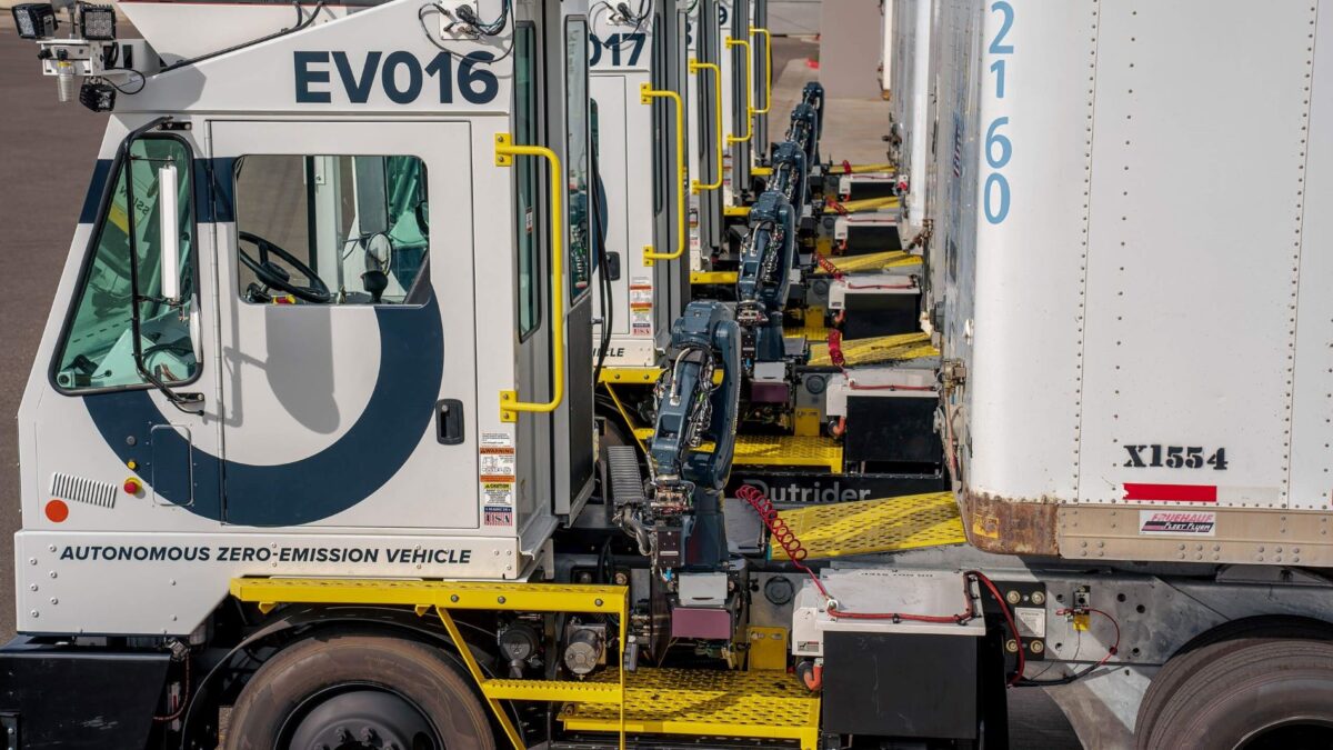 Electric Outrider yard trucks beside trailers, showing robotic trailer-connection equipment