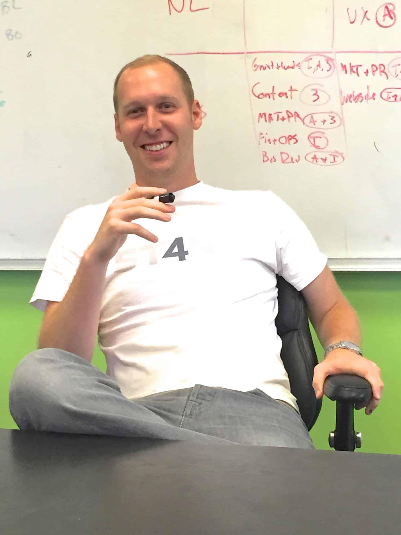 Andy Hill in a Stand4 T-shirt, seated beside a whiteboard covered in planning notes
