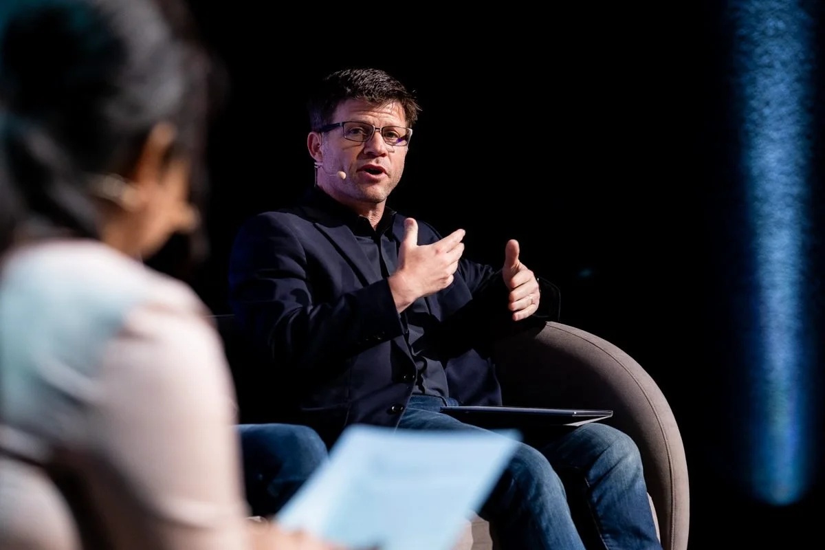 Andy Ruben, wearing glasses and a dark shirt, speaking with another participant during an on-stage conversation.
