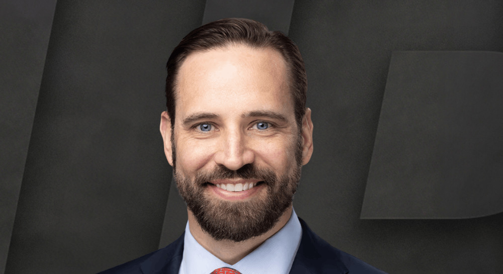 Andy Yakulis in a suit and tie against a dark geometric background