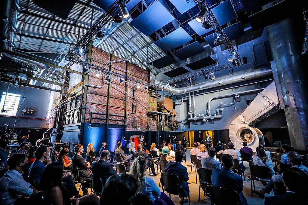 People seated at an event beneath industrial equipment at Instituto Caldeira