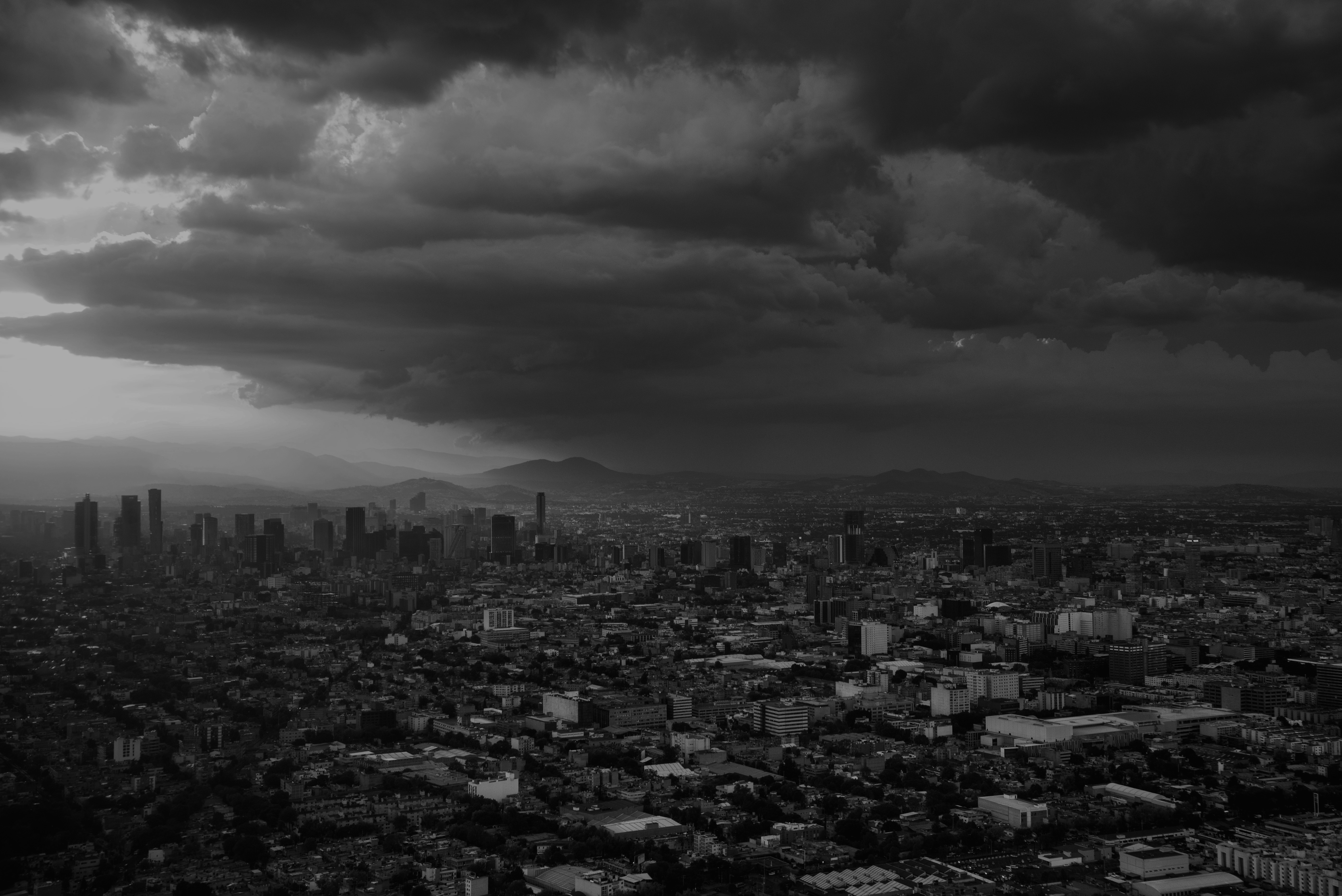 A dense cityscape beneath dark clouds, photographed in black and white