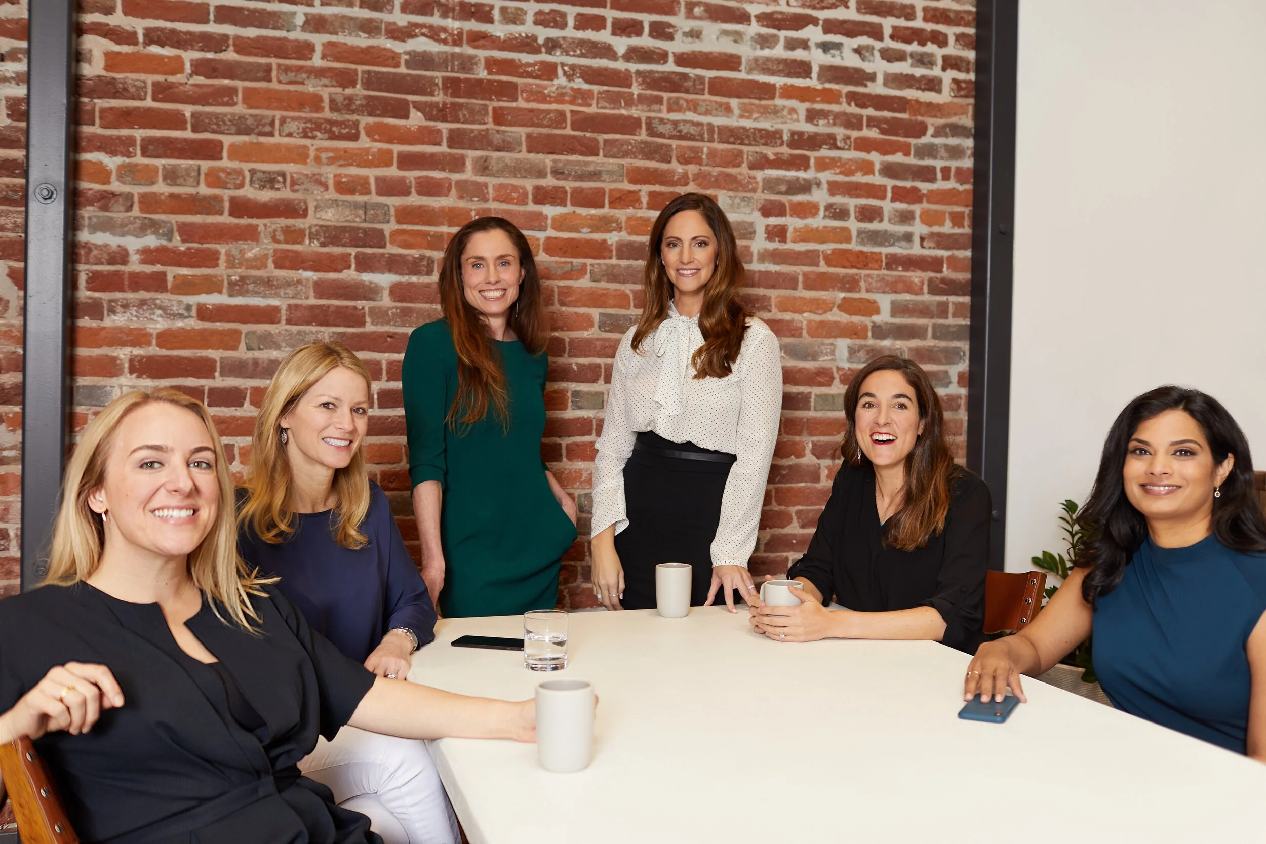 The six #ANGELS co-founders gathered around a table in front of a brick wall