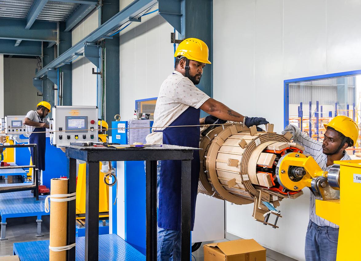 Workers handling a large coil assembly on a factory production line