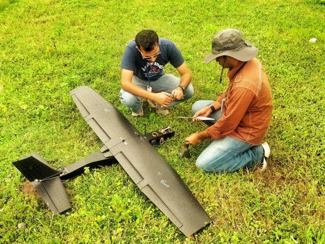 Two people working beside a fixed-wing unmanned aircraft on grass