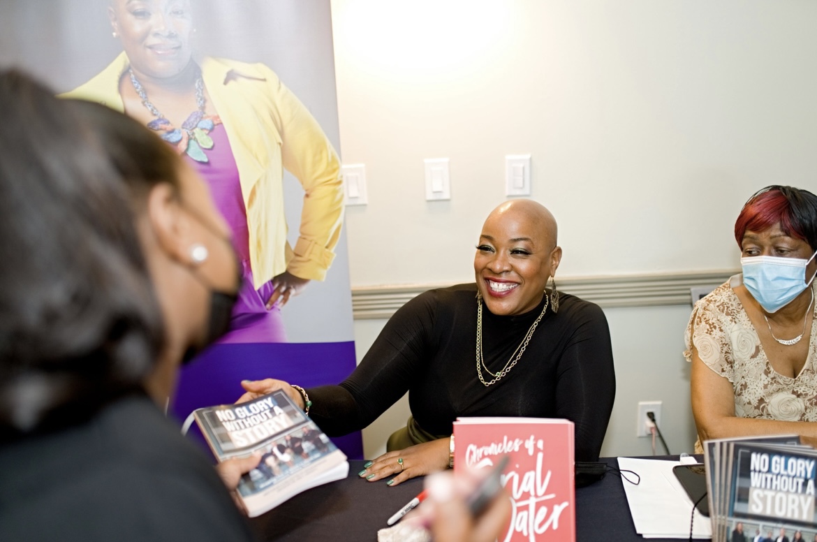 Ann Marie Sorrell smiles while speaking to a visitor at a table displaying her books