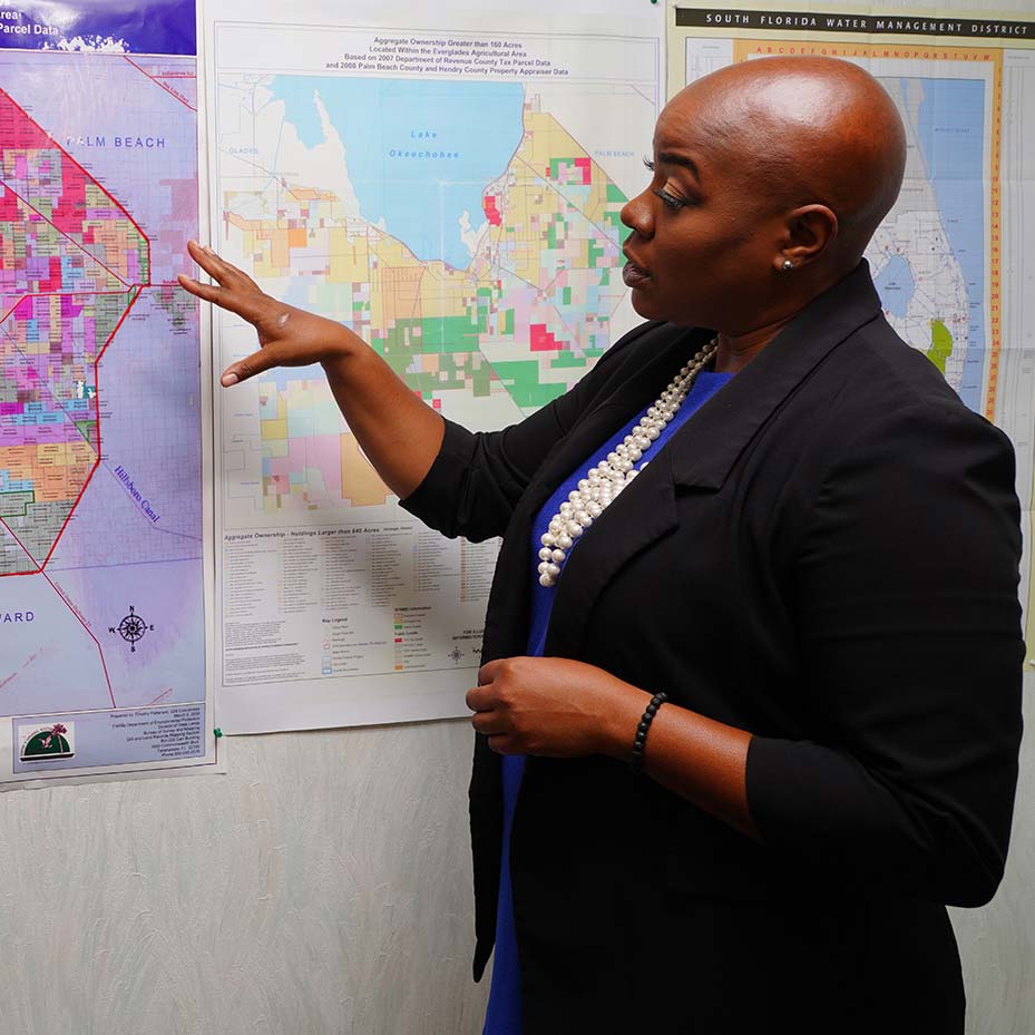 Ann Marie Sorrell gestures toward agricultural land-use maps beside a map of Lake Okeechobee