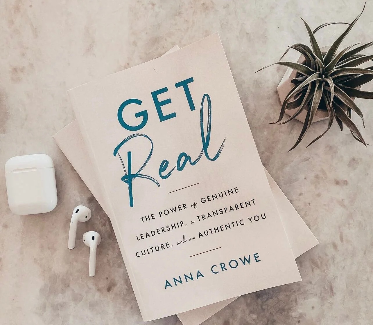 Anna Crowe’s book Get Real beside a pair of earbuds and a plant