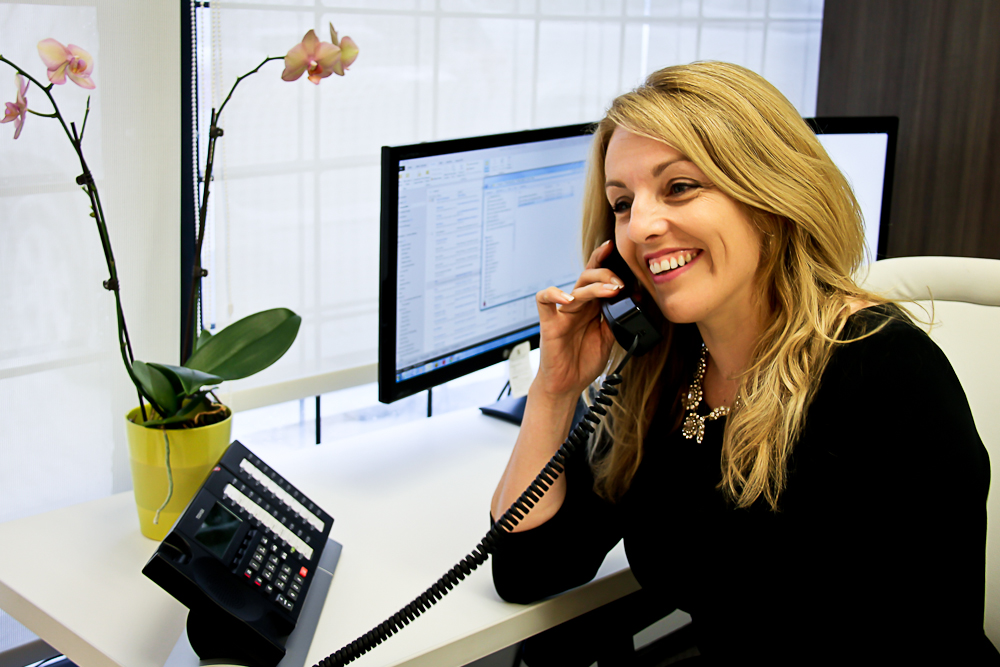Anne Whelan smiling while using a desk telephone in her office