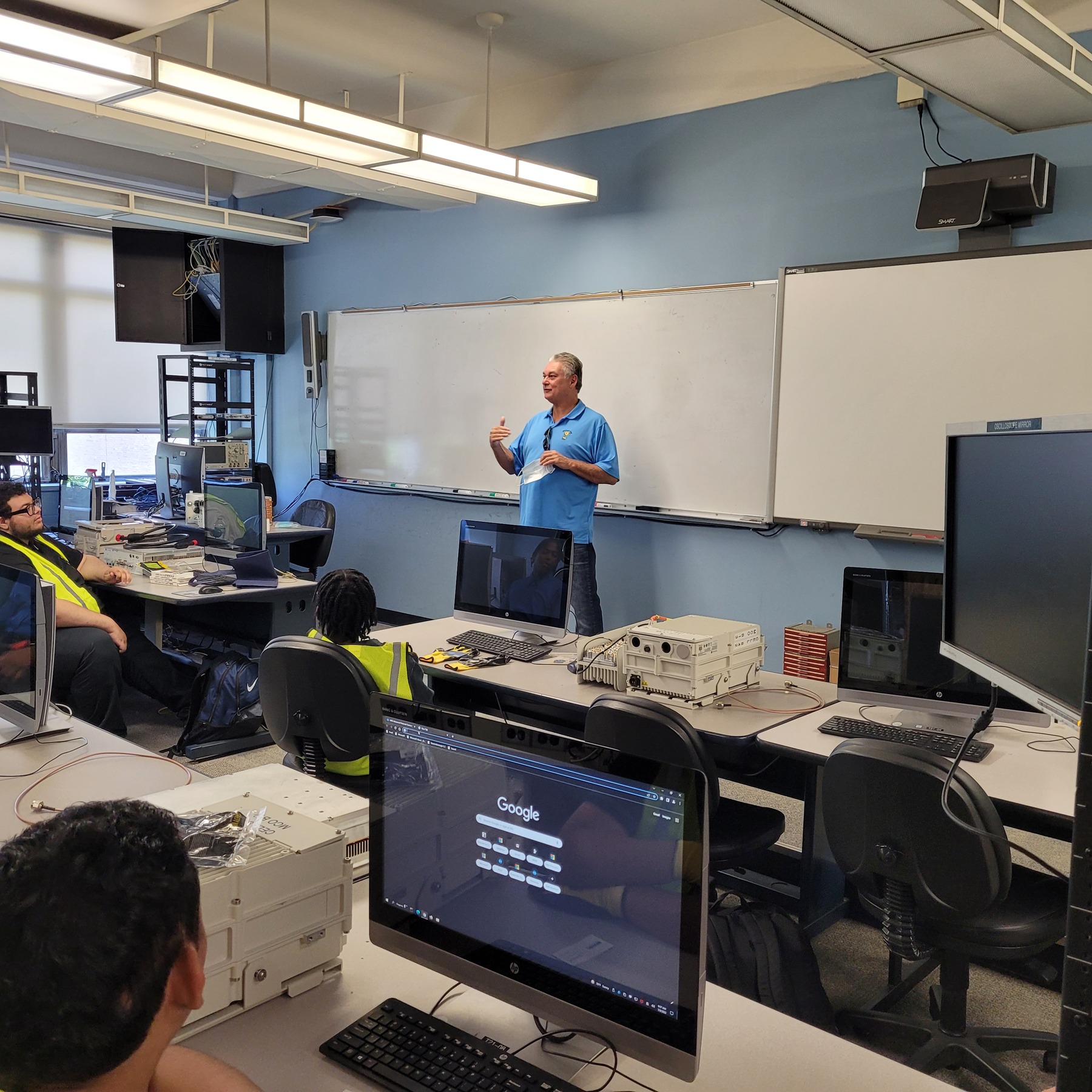 Paul Fettuccia speaking with students among telecom equipment at Queensborough Community College in July 2022