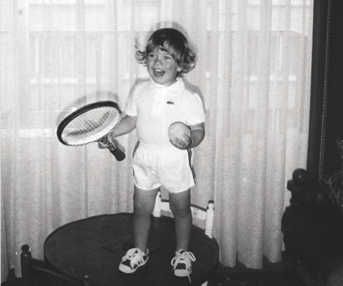 Anthony Evrard at age three, holding a tennis racket and ball in a Lacoste outfit
