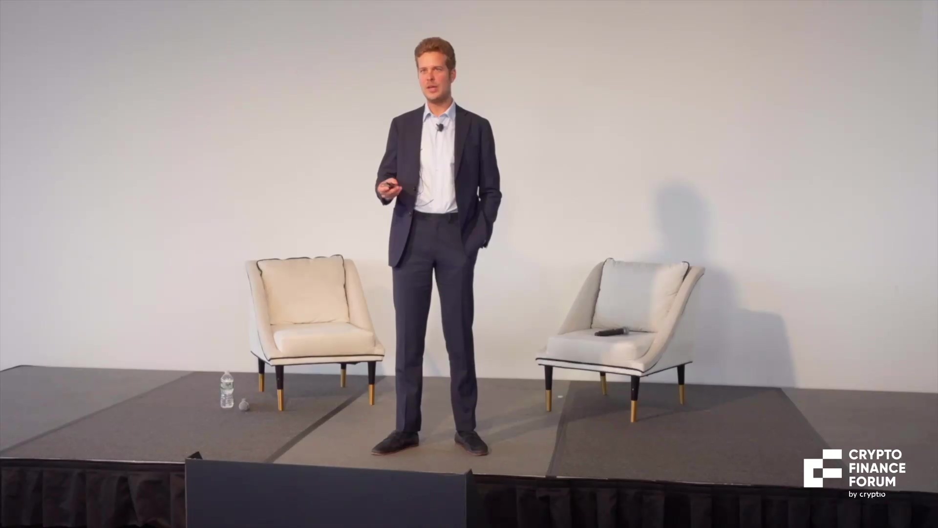 Antoine Scalia presenting on stage between two armchairs at Crypto Finance Forum.