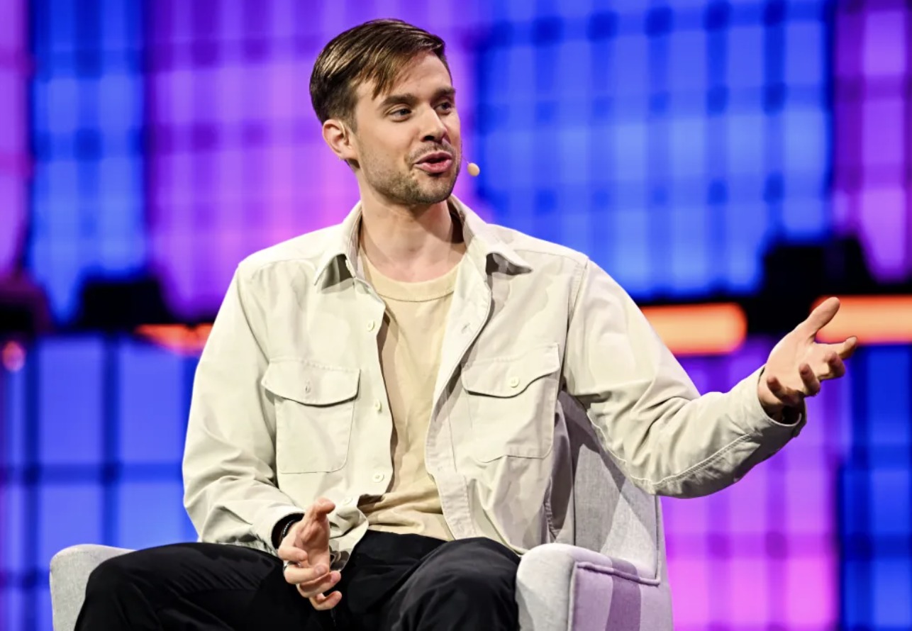Anton Osika speaking on stage, wearing a light shirt and gesturing during a conversation
