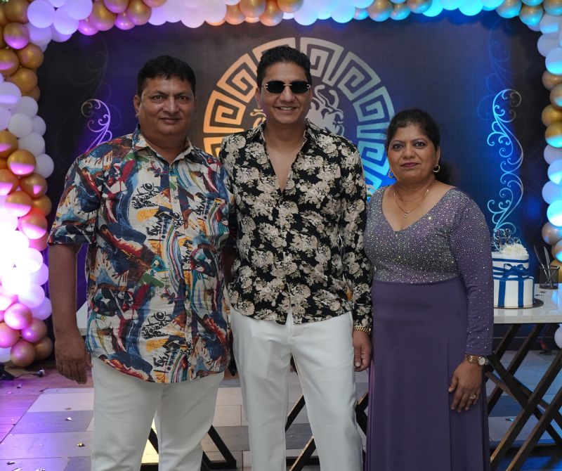 Pakhare in a floral shirt and sunglasses standing with two attendees at the anniversary celebration