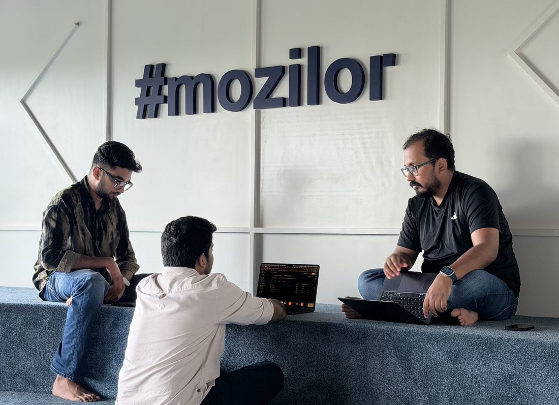 Three Mozilor team members discussing work with laptops beneath the company name