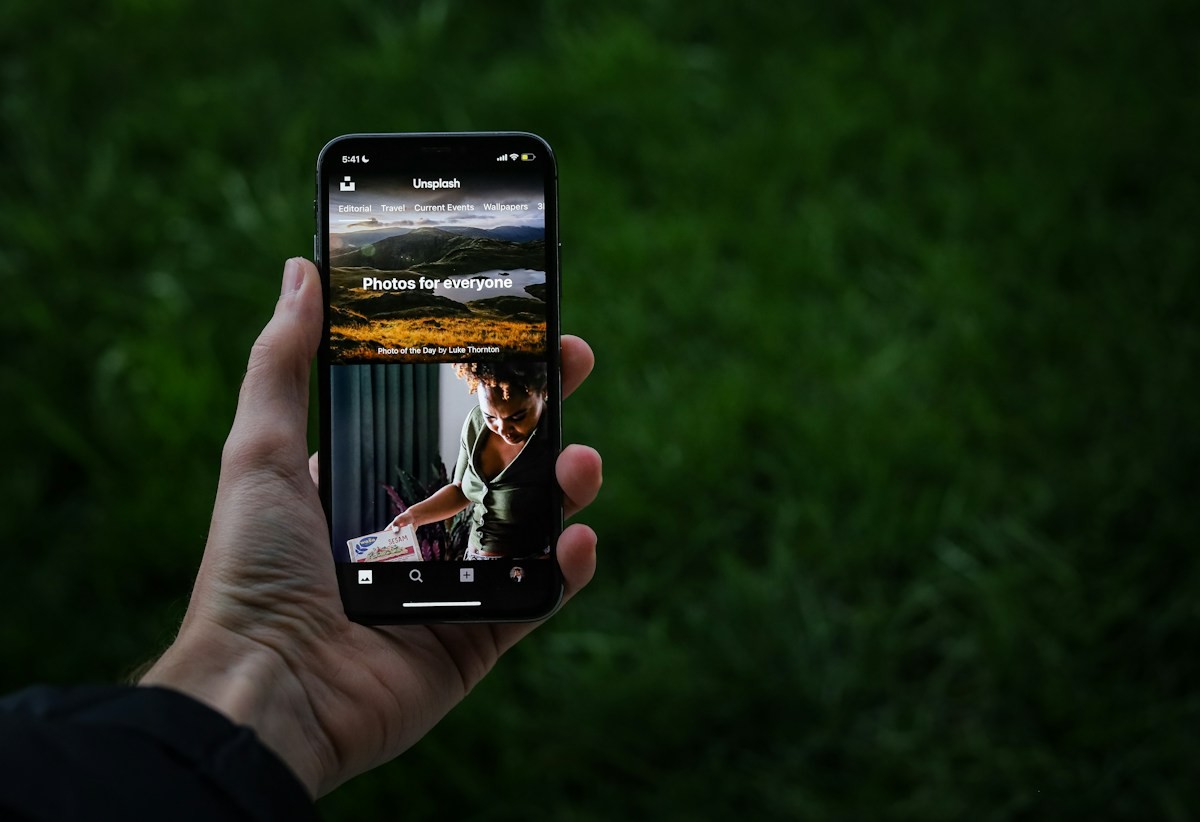 A hand holding an iPhone displaying the Unsplash app