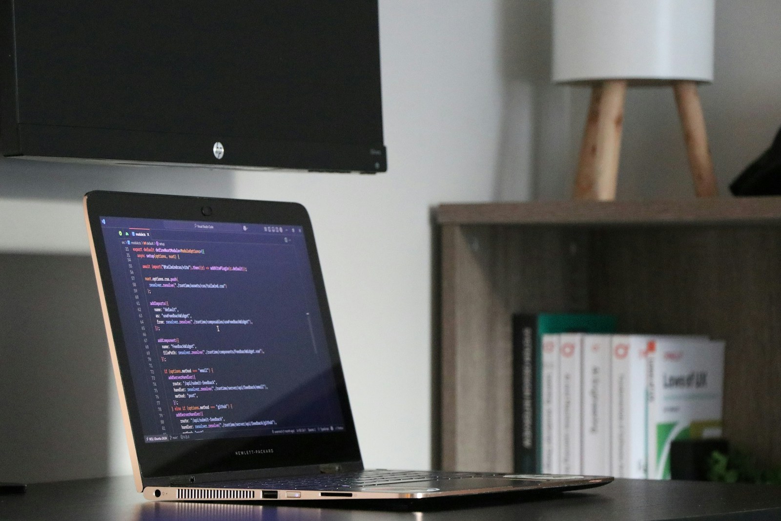 A laptop displaying source code on a desk beside a bookcase