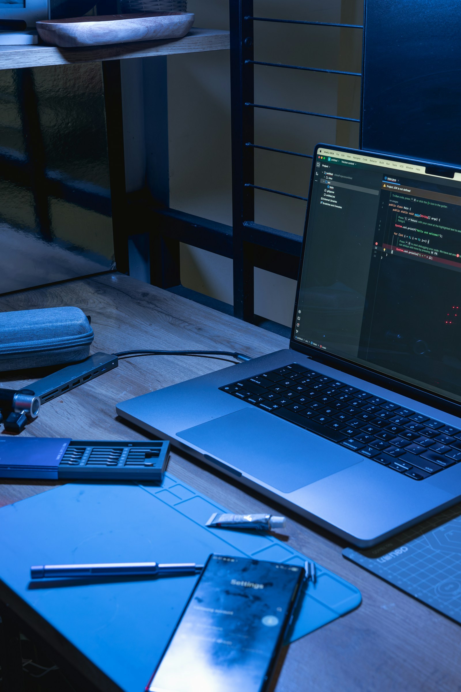 A laptop displaying code and a smartphone on a blue-lit desk