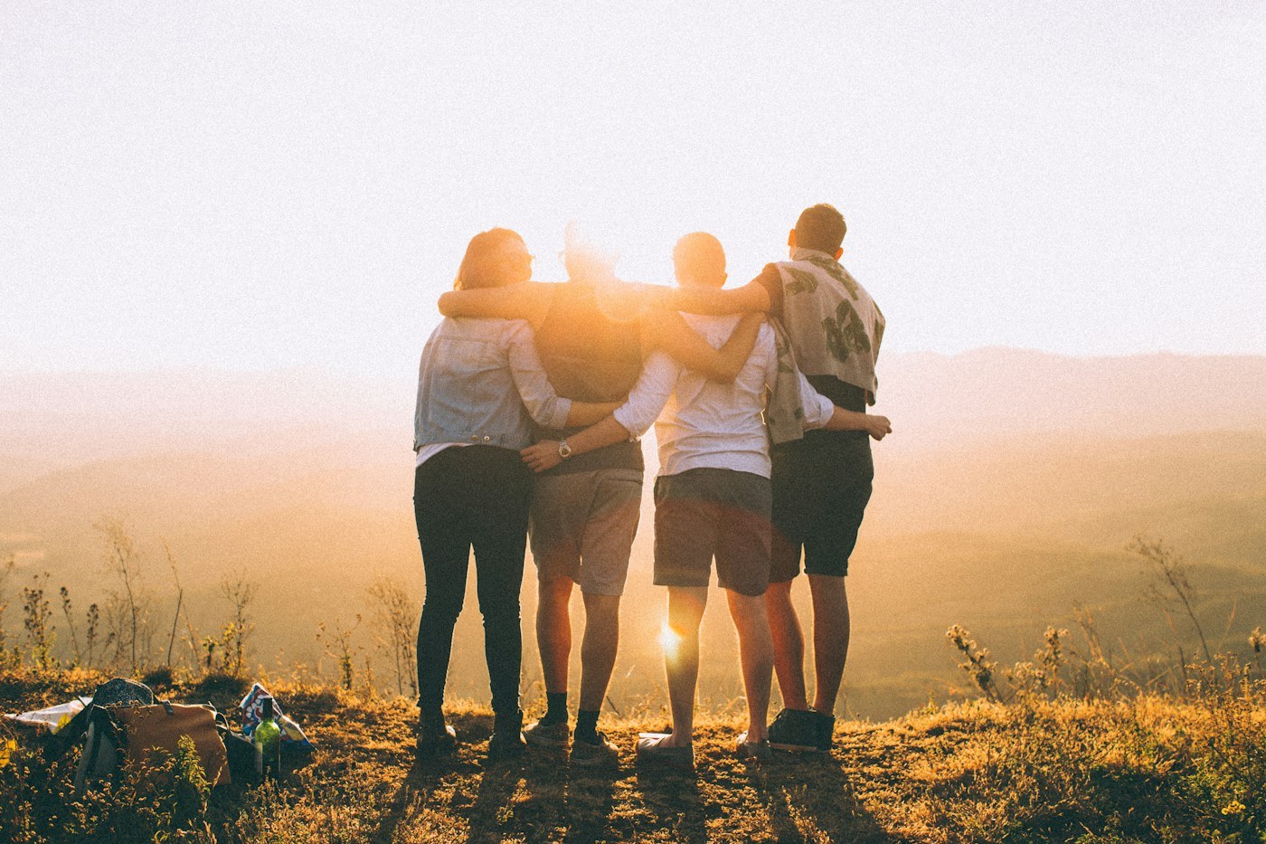 Four friends with their arms around each other on a sunlit hillside