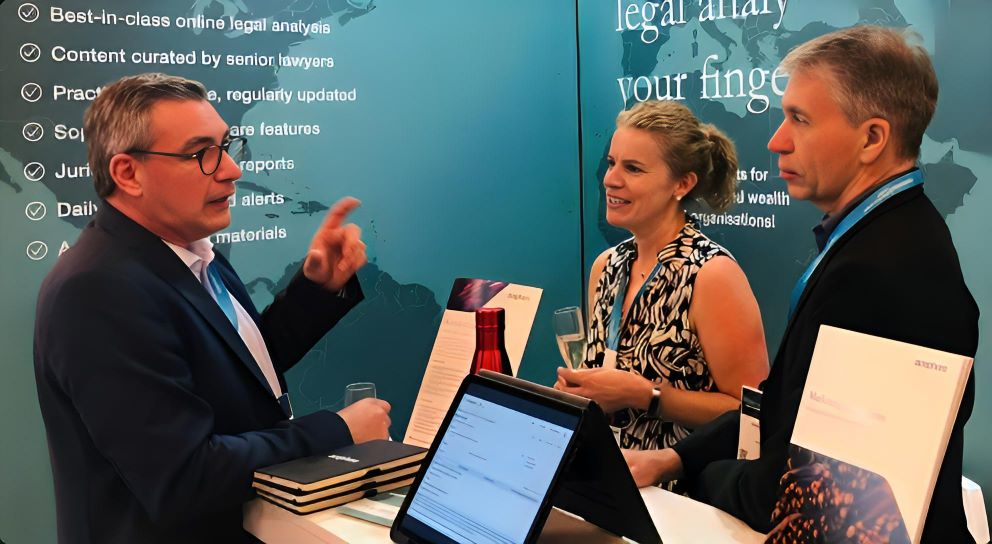 Three people talking at an aosphere exhibition stand beside a tablet displaying the platform