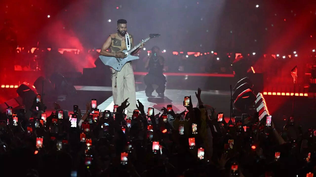 AP Dhillon performing under red stage lights before a large crowd