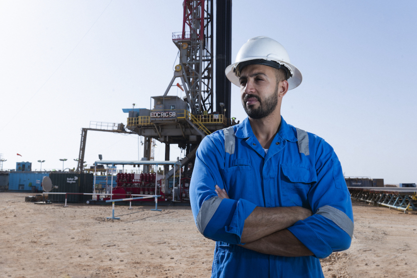 A worker in blue coveralls and a hard hat stands in front of a drilling rig in Egypt’s Western Desert