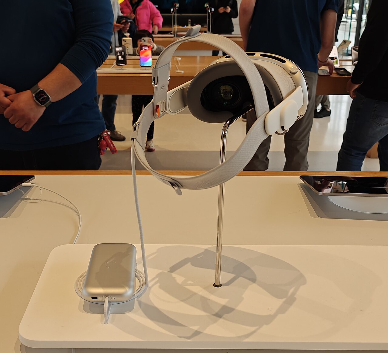 An Apple Vision Pro headset on a stand in an Apple Store, tethered to its battery pack