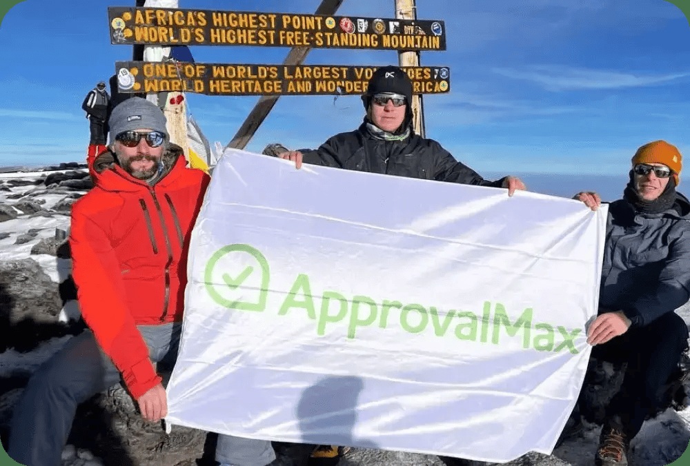 People at a mountain summit holding an ApprovalMax flag