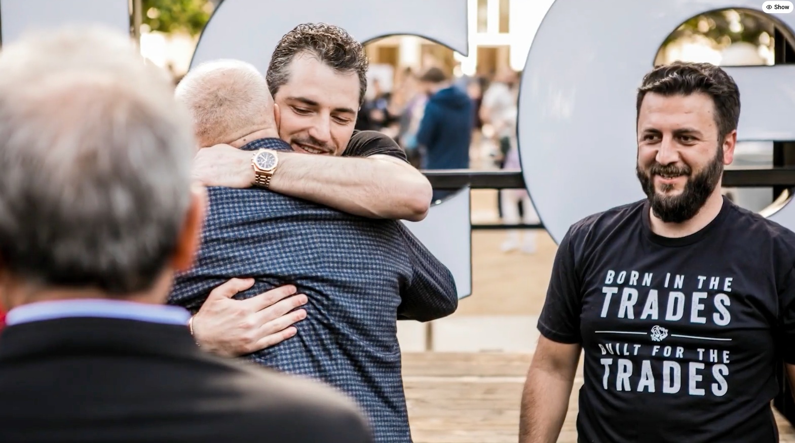 Ara Mahdessian embraces another attendee while Vahe Kuzoyan looks on, wearing a Born in the Trades T-shirt.