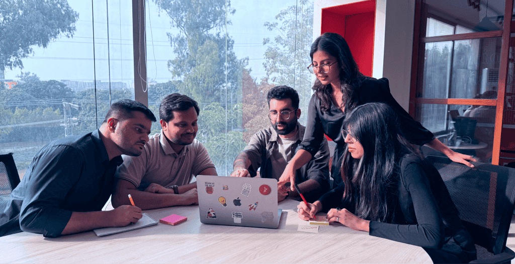 Five Arbisoft colleagues discussing work around a laptop in a bright office
