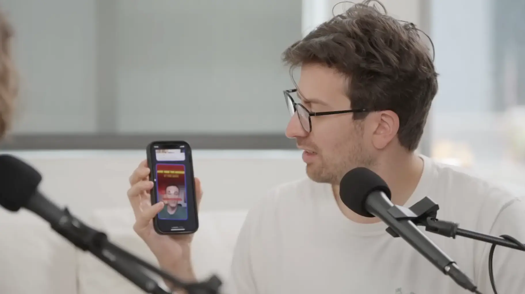 A podcast host holding up a phone displaying a vertical video in footage featured by Arcads