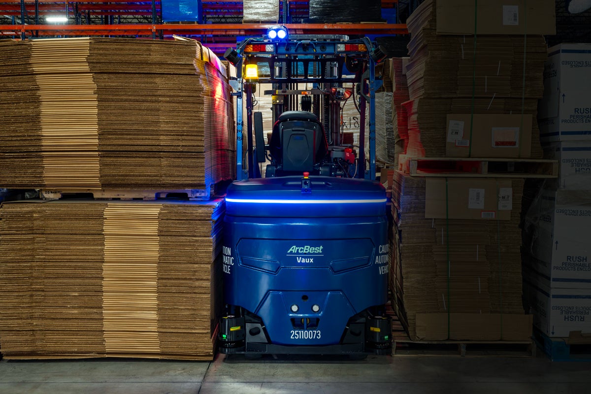 A blue Vaux autonomous forklift standing between stacks of warehouse freight