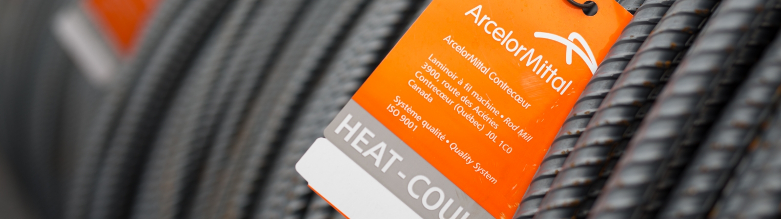Coiled steel rod carrying an orange ArcelorMittal quality tag