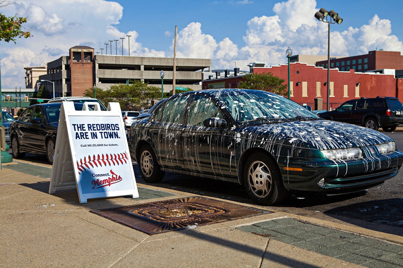 A car covered in simulated bird droppings beside a sign announcing the Memphis Redbirds