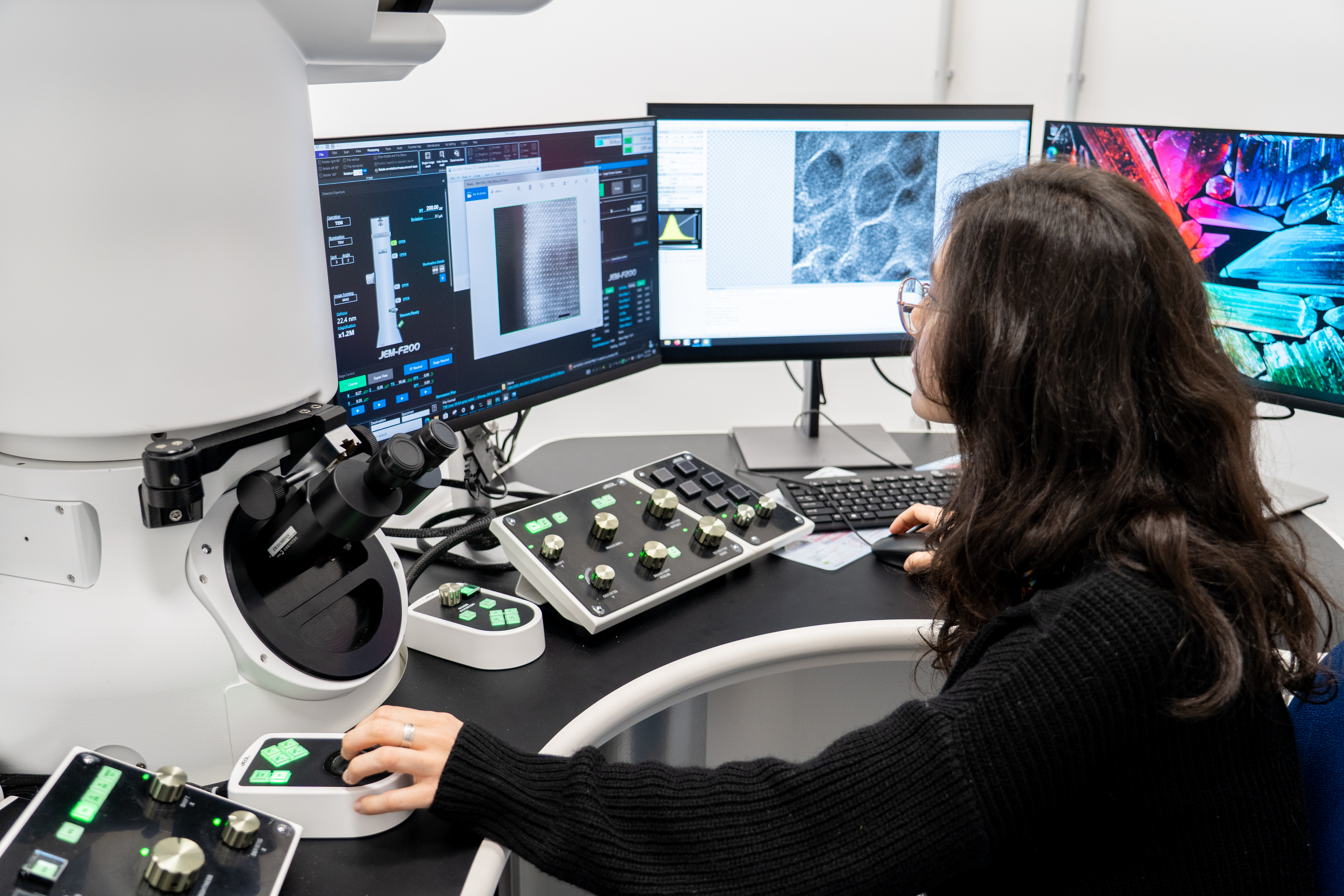 Researcher operating an electron microscope with three imaging monitors at Area Science Park’s LAME laboratory