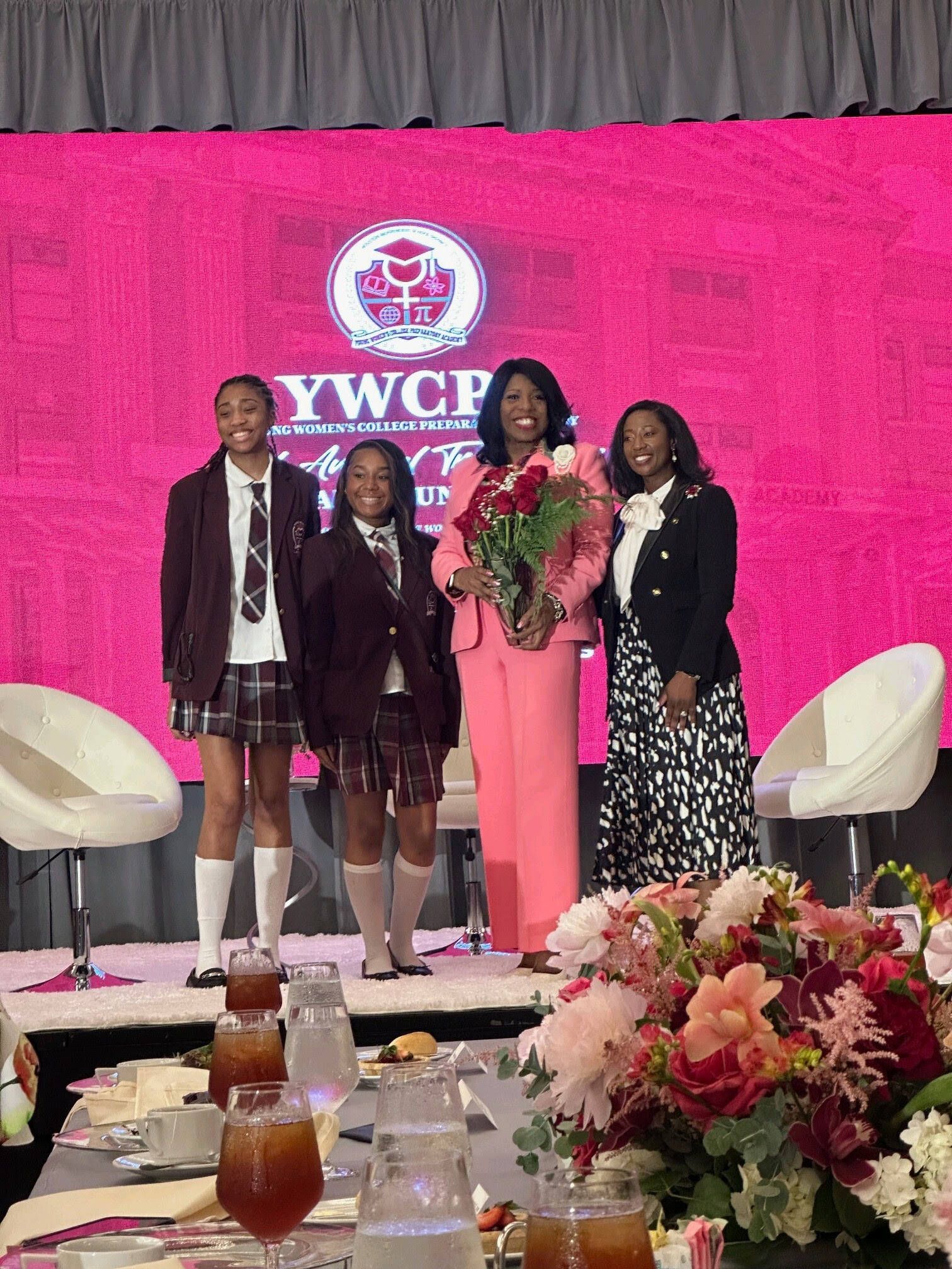 Argentina James in a pink suit, holding flowers beside two YWCPA students and principal Tabitha Davis at the 2024 Trailblazer luncheon