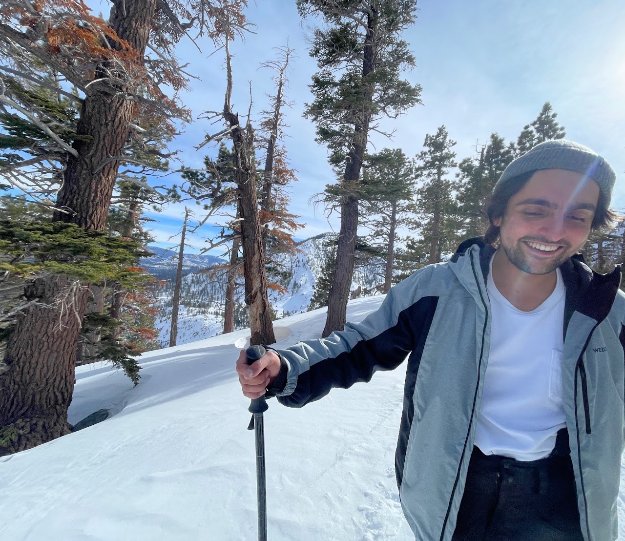 Ari Malik smiling outdoors among snow-covered trees, holding a pole