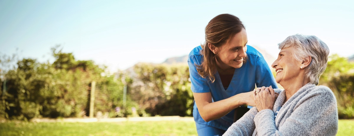 A clinician speaking warmly with an older woman seated outdoors