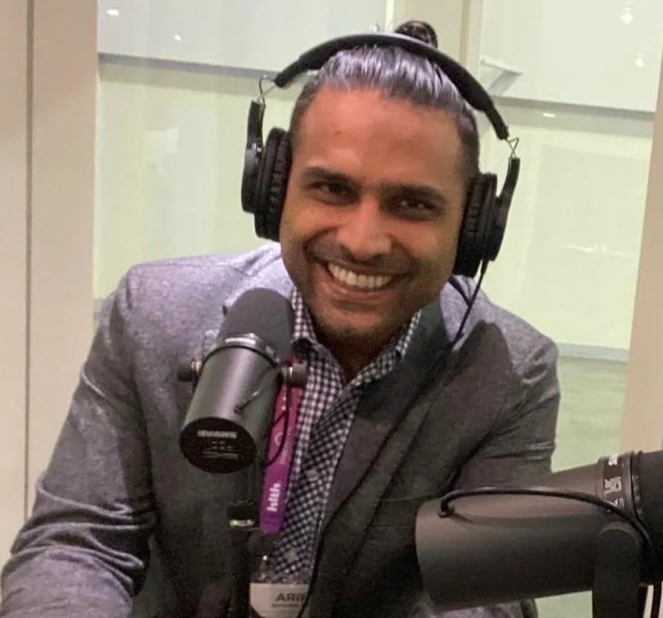 Arif Nathoo smiling at a microphone while wearing headphones during an interview
