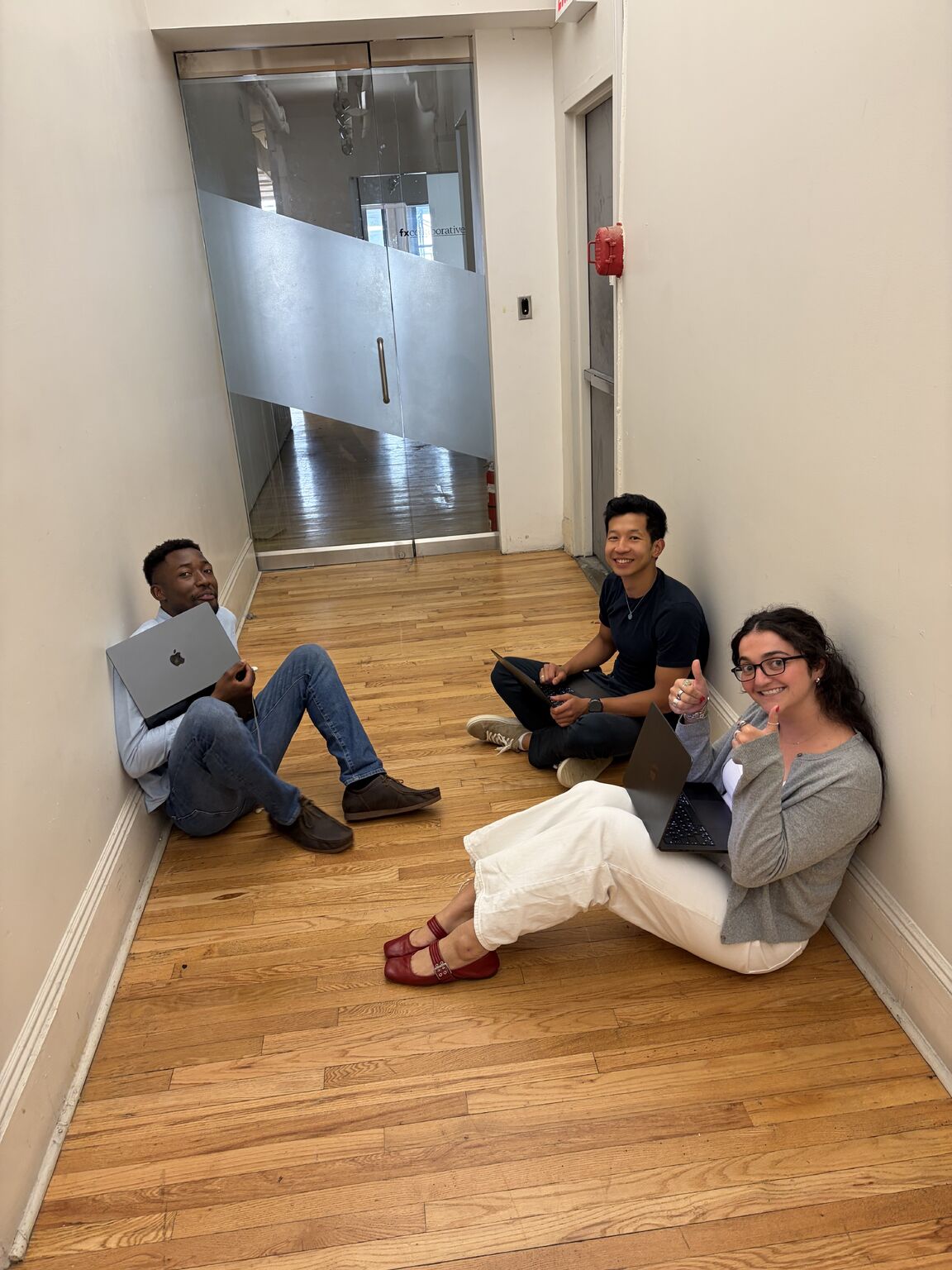 Three Solstice colleagues, including co-founder Yiwen Li, seated in a wooden-floored office hallway with open laptops
