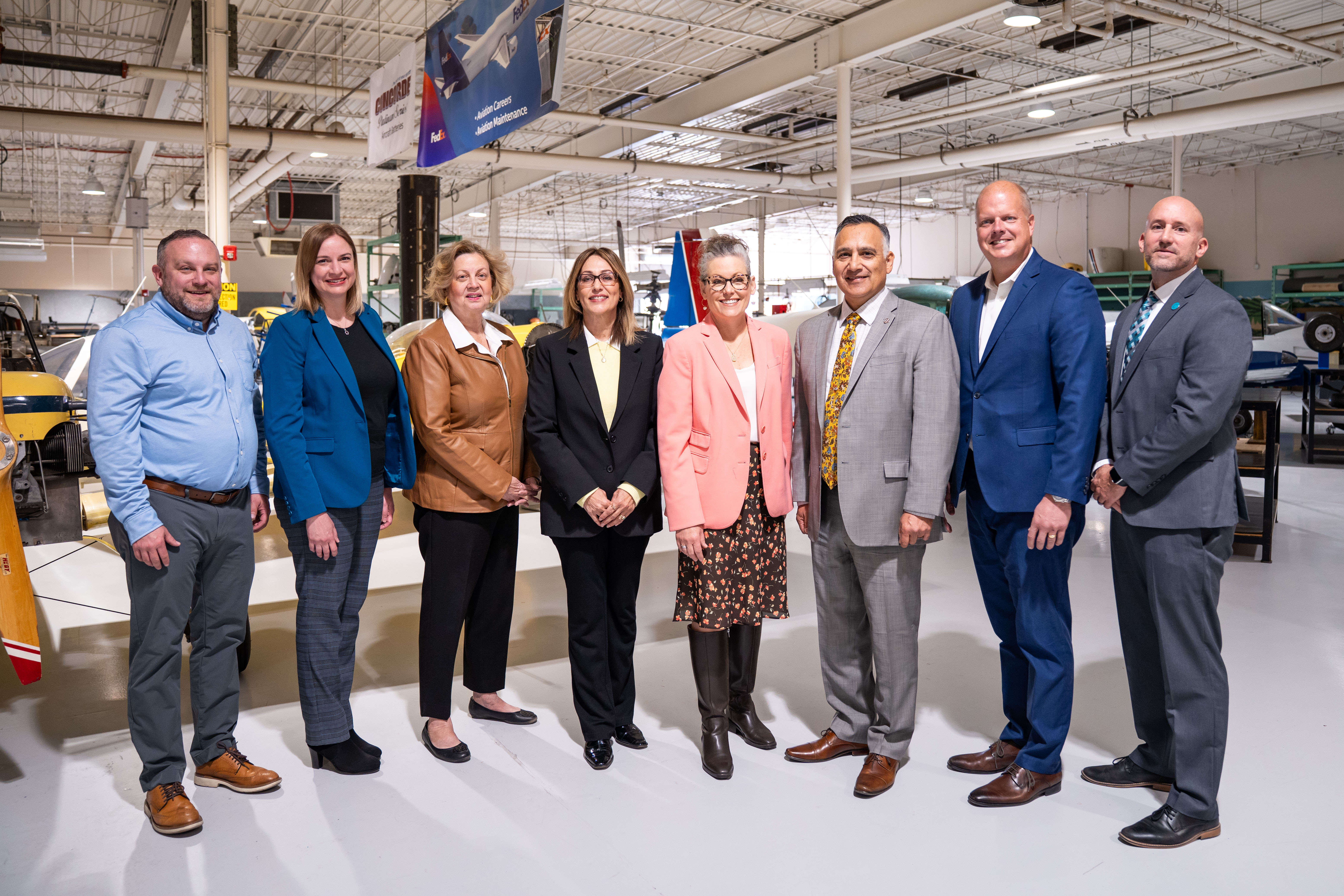 State, college, and aerospace industry partners stand beside training aircraft at the Mesa workforce accelerator announcement