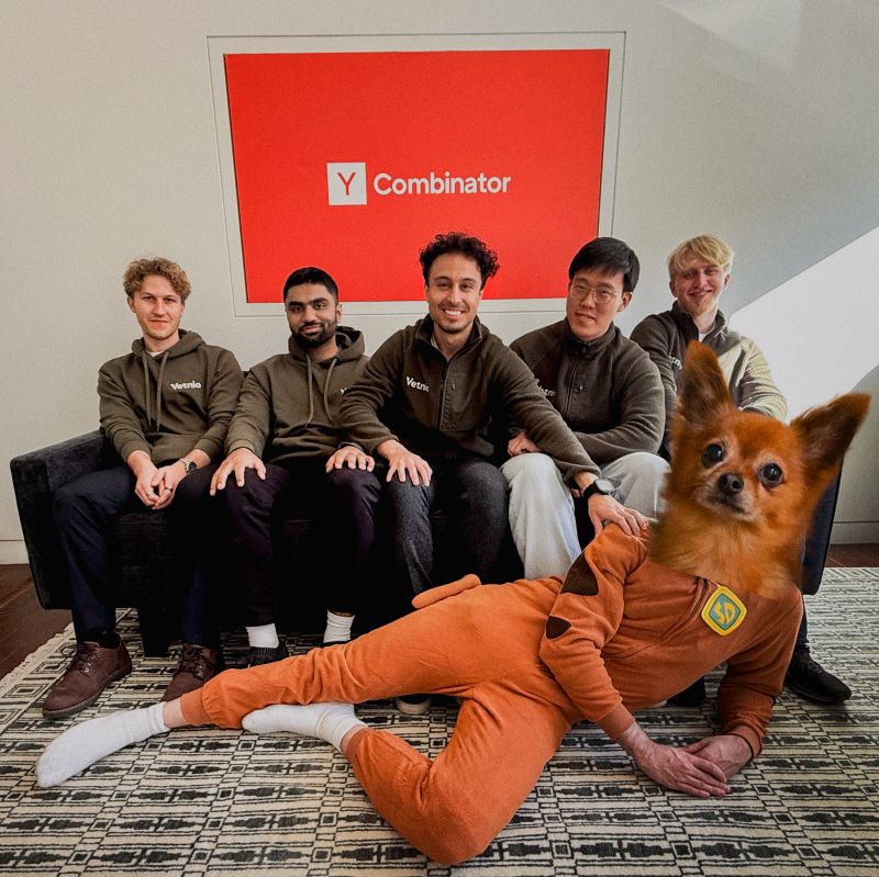 Arman Karégar seated with the Vetnio team beneath a Y Combinator sign while a playful dog-costume figure reclines in front