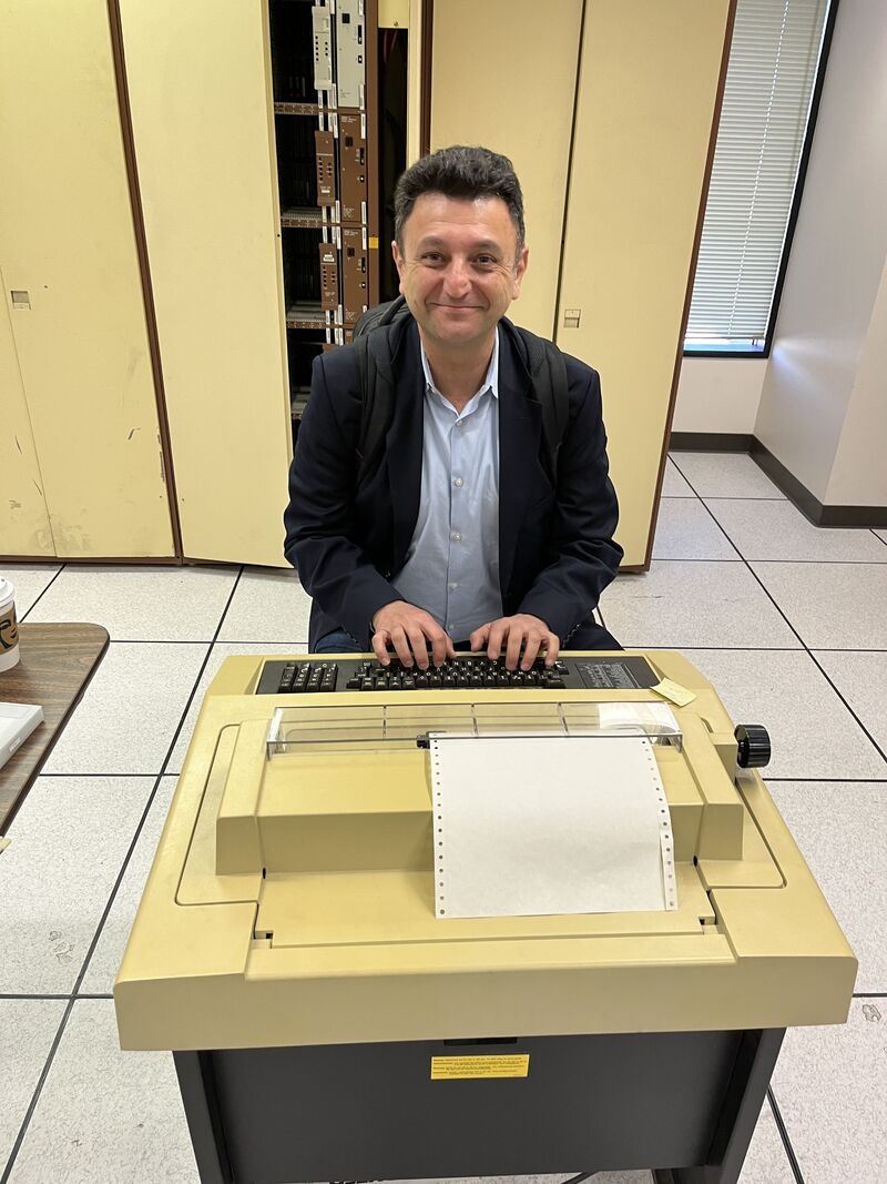 Arman Khalili smiling at a vintage beige terminal with continuous-feed paper